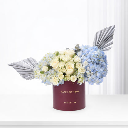 Elegant white roses, blue hydrangeas, silver foliage in burgundy "Happy Birthday" box, minimalist luxury floral gift.