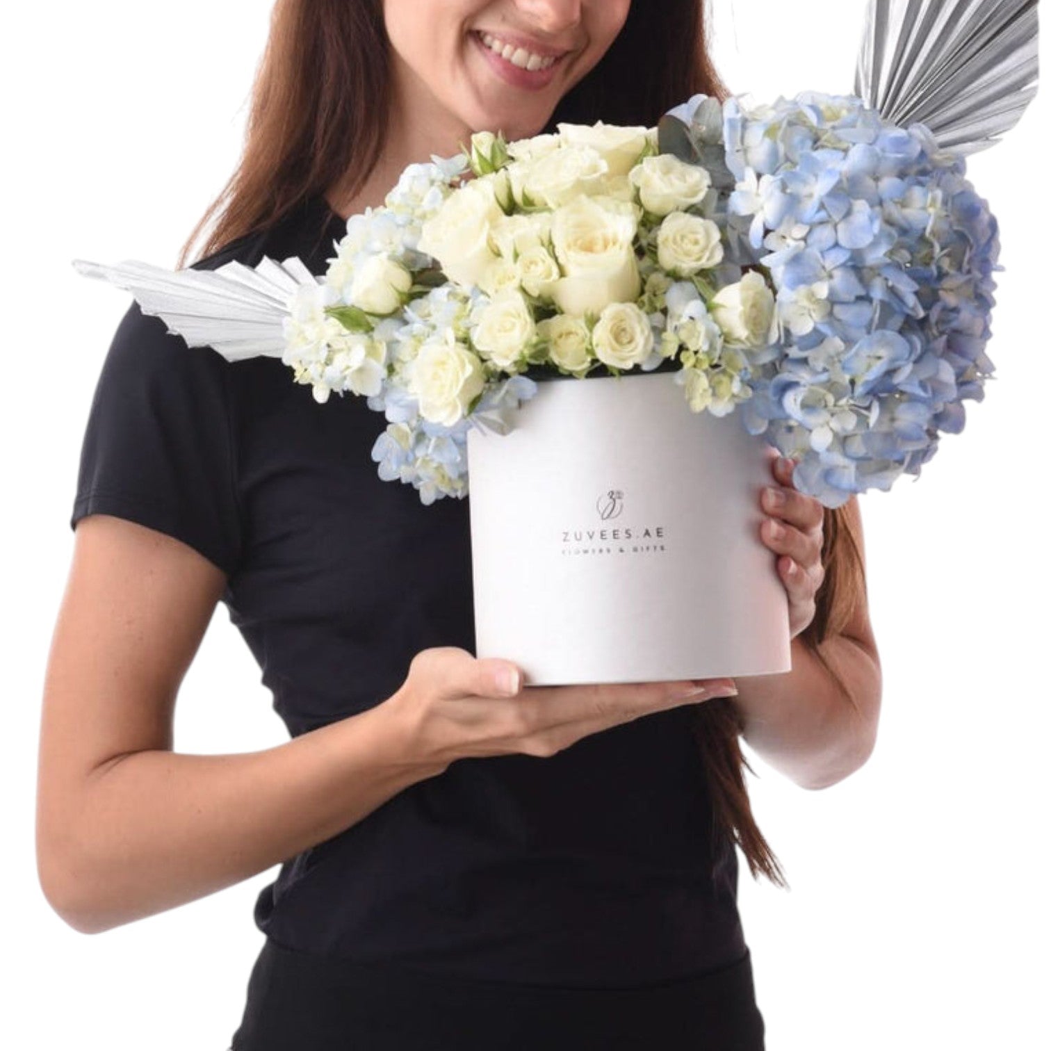 White box holds creamy roses and blue hydrangeas, accented with silver feather wings.