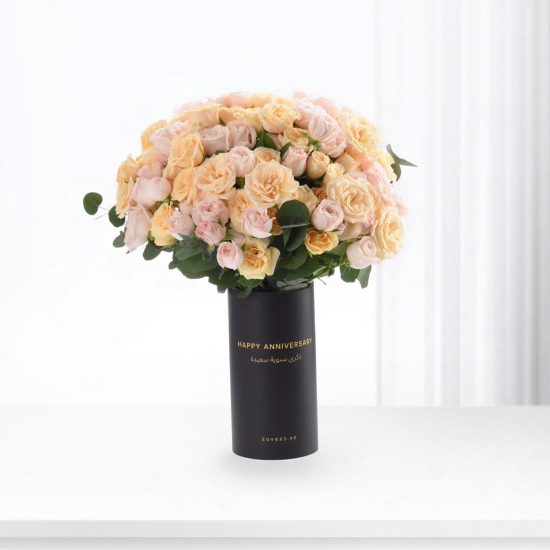 Soft peach roses in matte black vase with gold anniversary message.