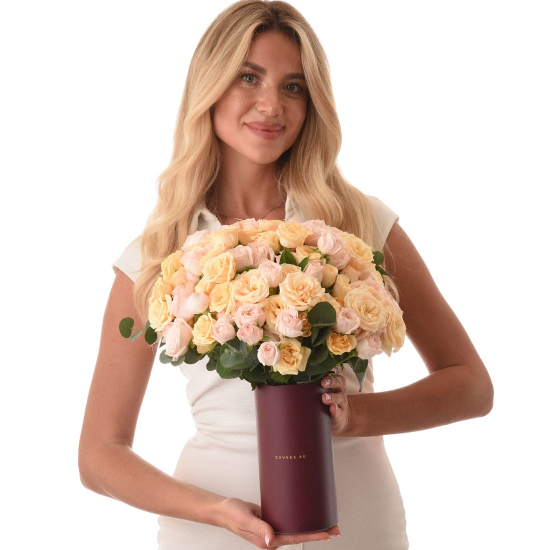 Blonde woman holds lush peach rose bouquet in burgundy vase.