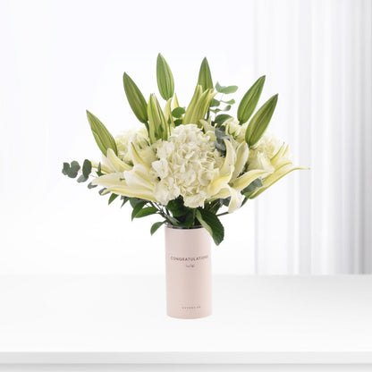 Elegant white lilies, hydrangeas, and buds in blush vase with "Congratulations" text.