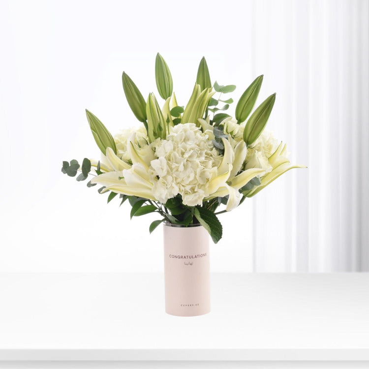 Elegant white lilies, hydrangeas, and buds in blush vase with "Congratulations" text.