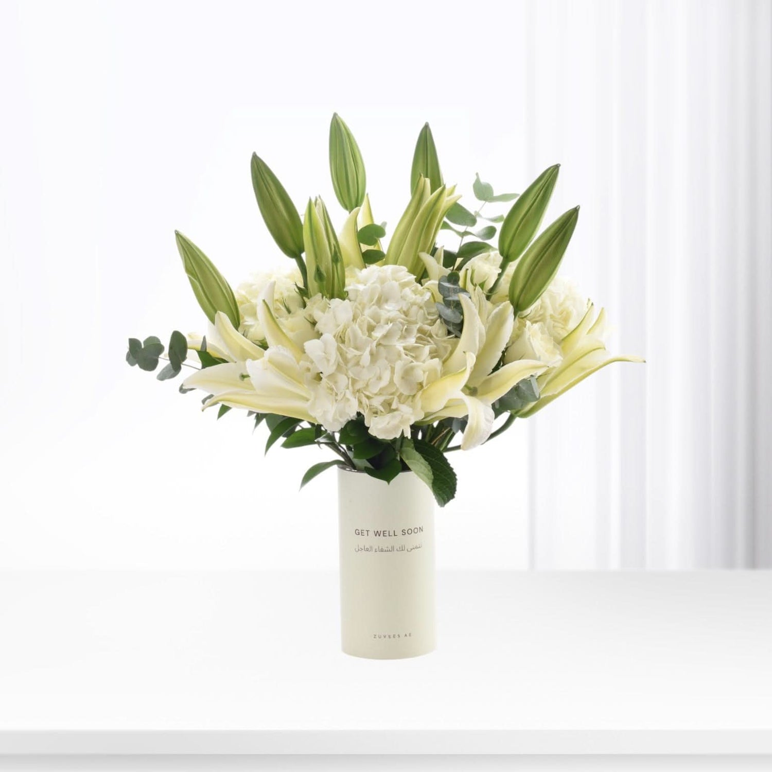 White lilies, hydrangeas, and buds in minimalist vase with "Get Well Soon" message.
