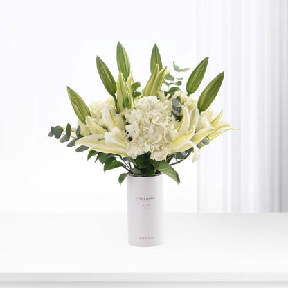 White vase holds creamy lilies, hydrangeas, and buds; minimalist, elegant apology bouquet.