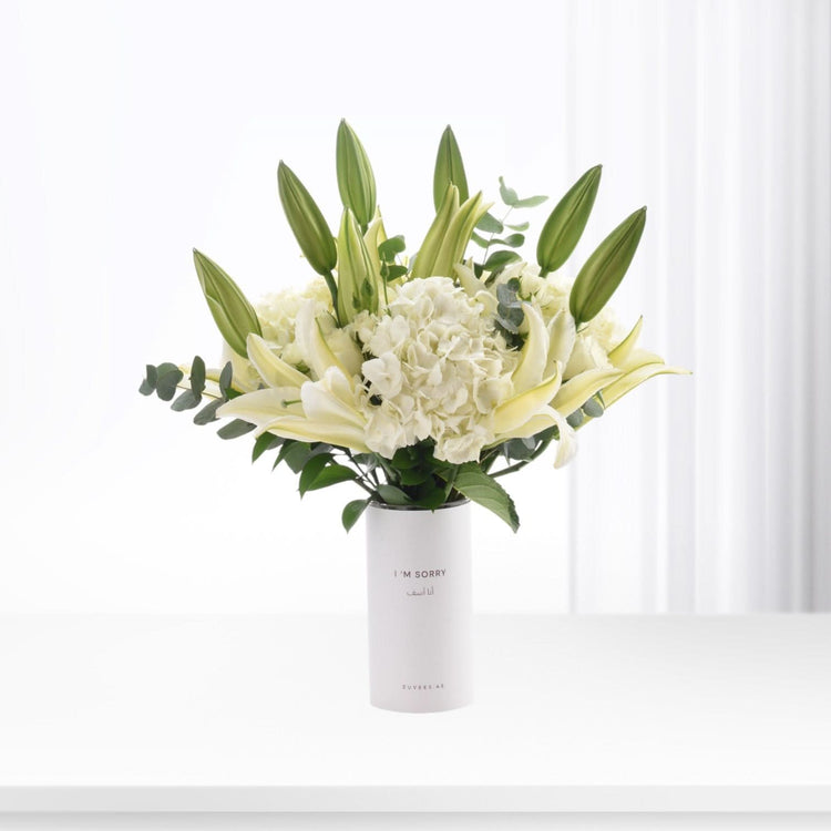 White vase holds creamy lilies, hydrangeas, and buds; minimalist, elegant apology bouquet.