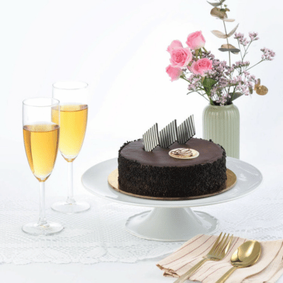 Rich chocolate cake with gold accents, champagne, pink roses, elegant table setting.