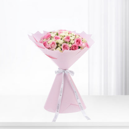 Soft pink roses and cream blooms elegantly wrapped in pastel pink paper with branded white ribbon.