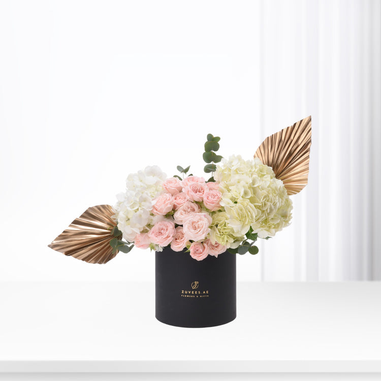Elegant black vase holds blush roses, white hydrangeas, and gold fan leaves.