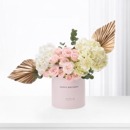 Pink roses and hydrangeas in blush box with gold leaves, "Happy Birthday" text.