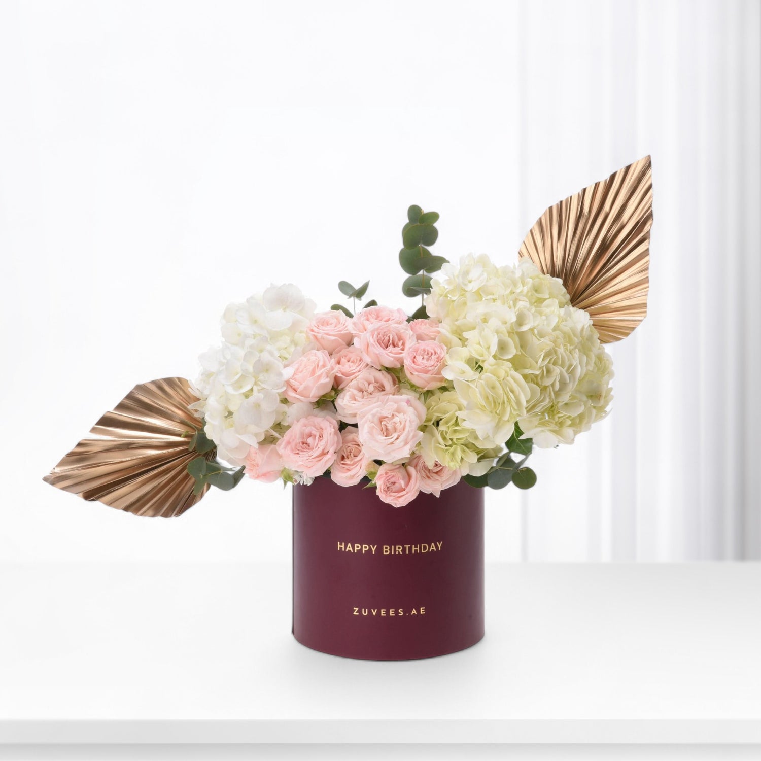 Elegant burgundy box holds blush roses, hydrangeas, and gold fan leaves for birthday.