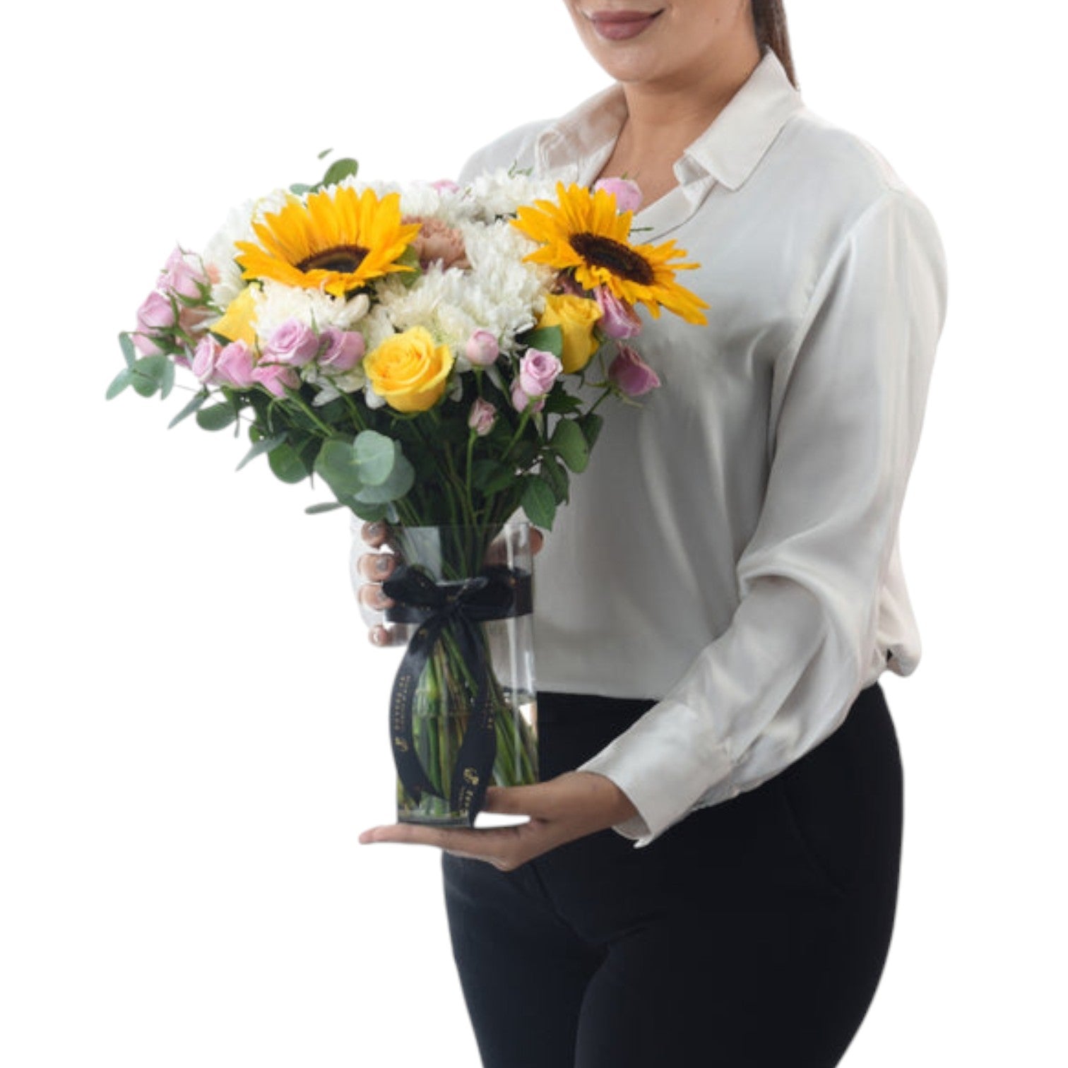 Woman holds vibrant sunflower, rose, and chrysanthemum bouquet in clear vase with black ribbon.