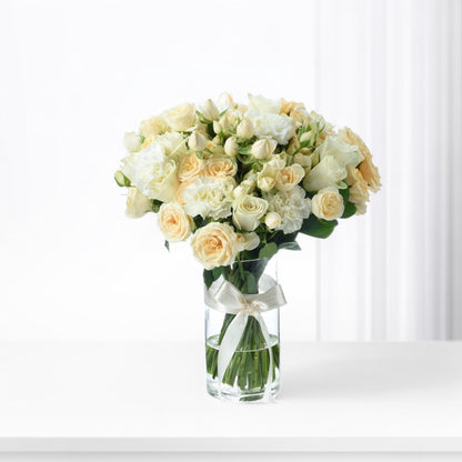 Elegant white and cream roses and carnations in clear vase with satin bow.
