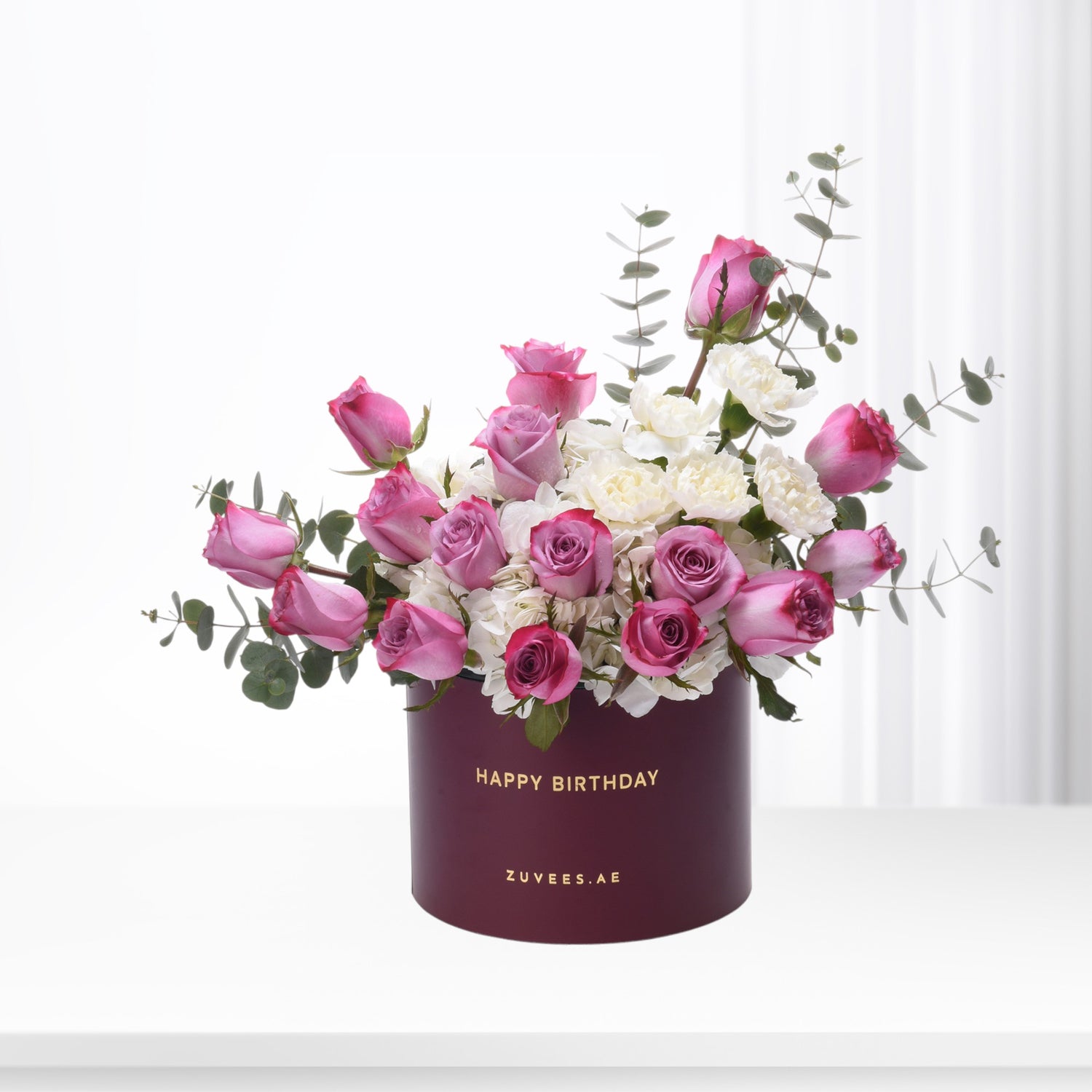 Elegant burgundy box with "Happy Birthday" holds pink roses and white blooms, accented with eucalyptus.
