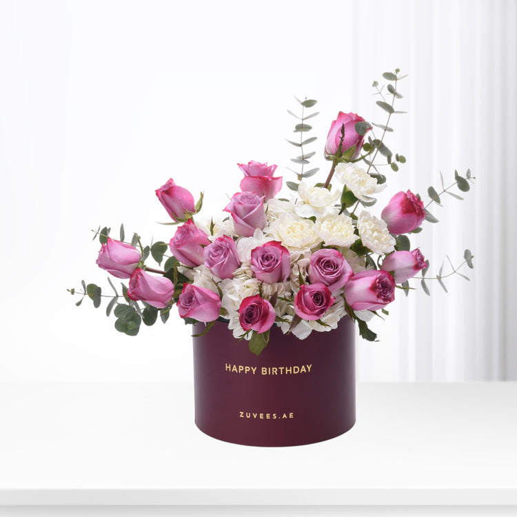 Elegant burgundy box with "Happy Birthday" holds pink roses and white blooms, accented with eucalyptus.
