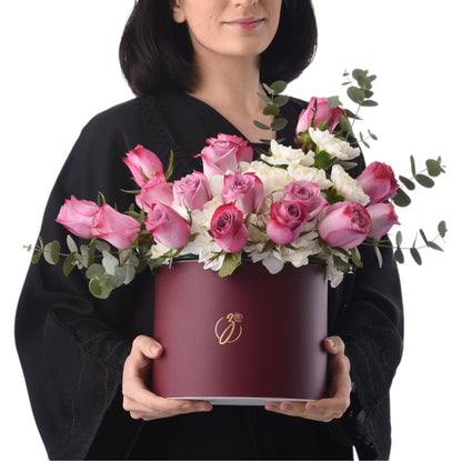 Woman holds burgundy hat box filled with pink roses and white blooms.
