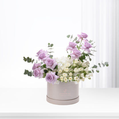 Lavender roses, white hydrangeas, and eucalyptus in elegant beige box, soft pastel floral gift.