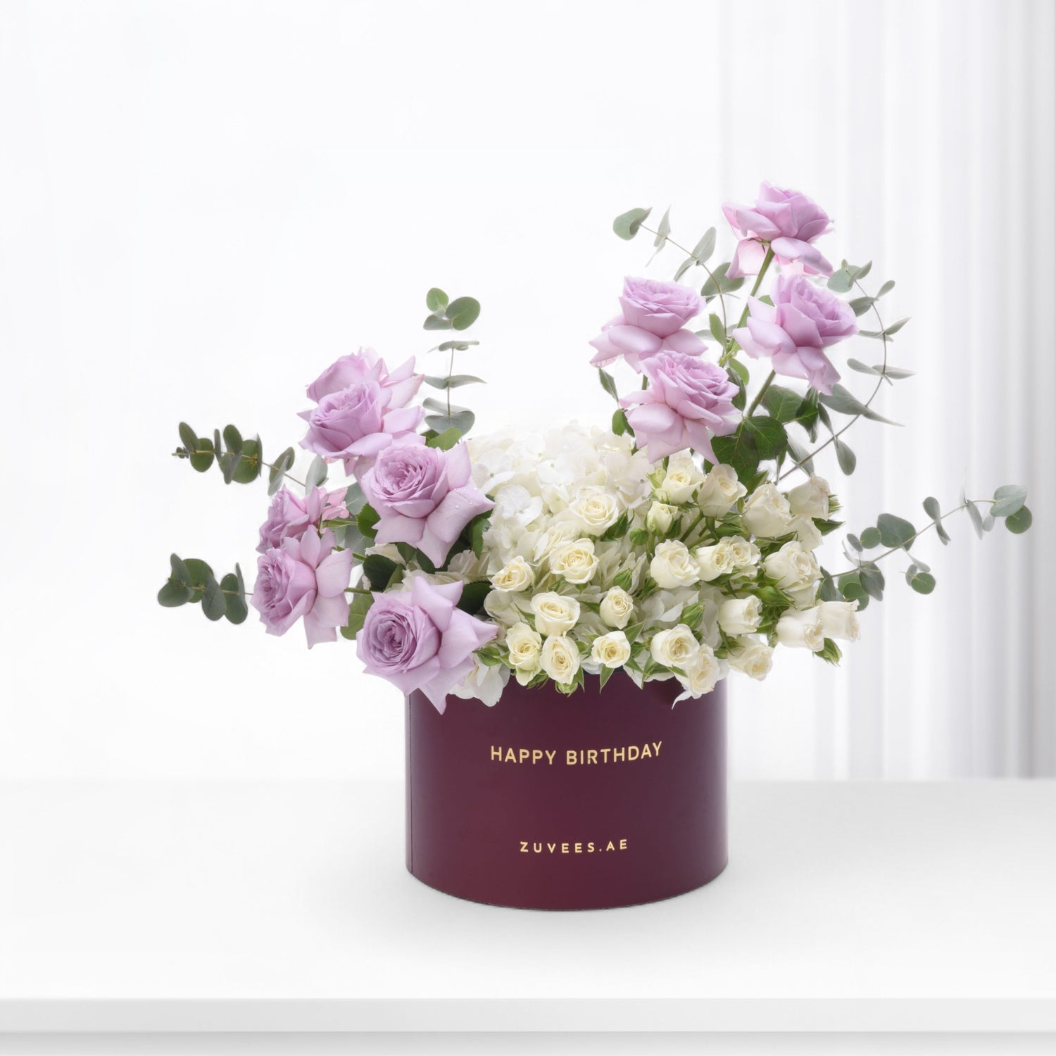 Elegant lavender roses and white blooms in burgundy birthday box.