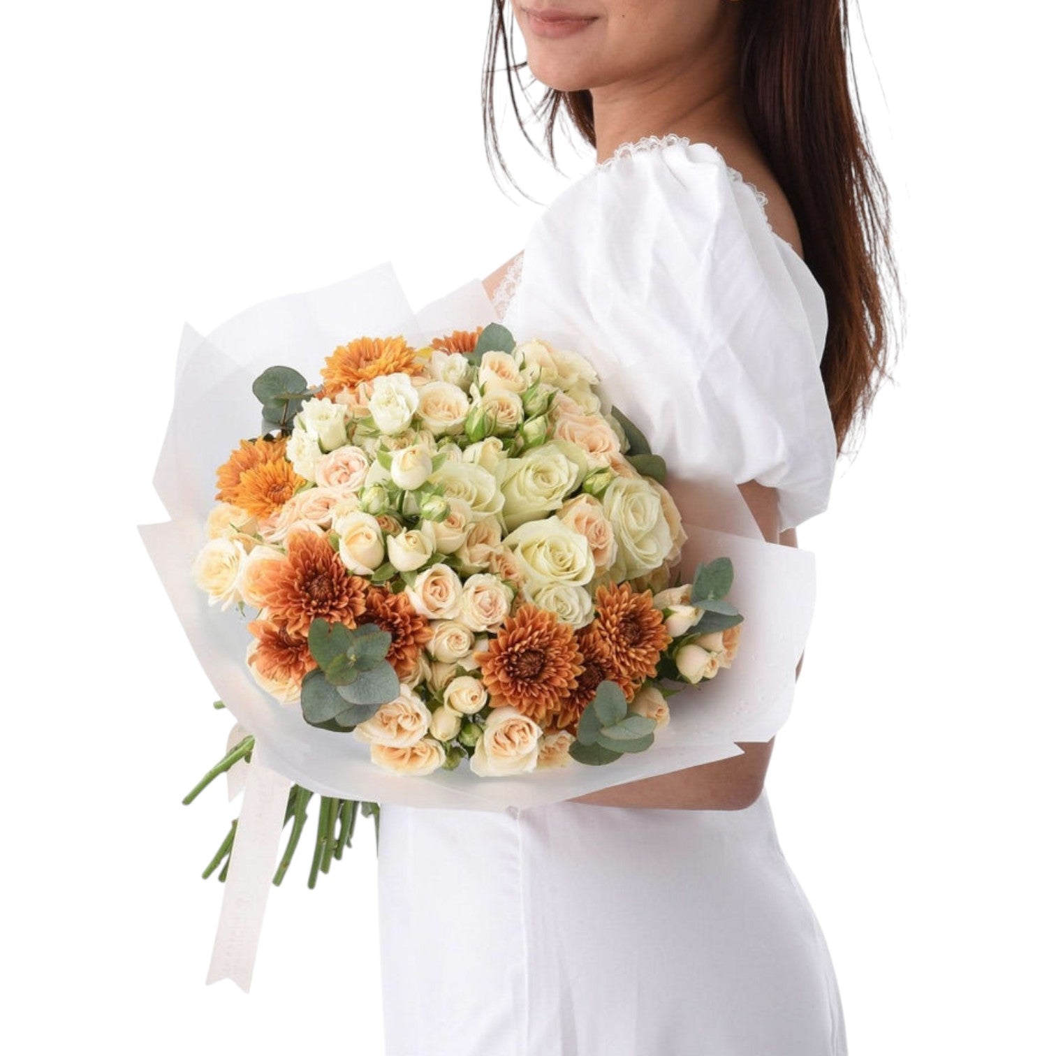 Woman holds vibrant orange and cream rose bouquet with eucalyptus, wrapped in white paper.