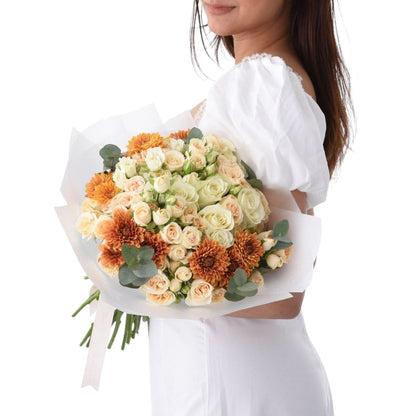 Woman holds vibrant orange and cream rose bouquet with eucalyptus, wrapped in white paper.