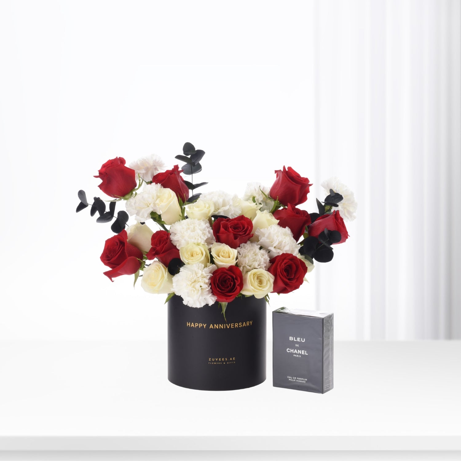 Elegant red, white roses and eucalyptus in black "Happy Anniversary" vase beside Chanel Bleu de Chanel perfume.