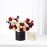Elegant red, white roses and eucalyptus in black "Happy Anniversary" vase beside gold-embossed gift box.