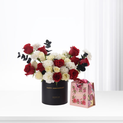 Elegant red, white roses and carnations in black "Happy Anniversary" vase with pink floral gift box.