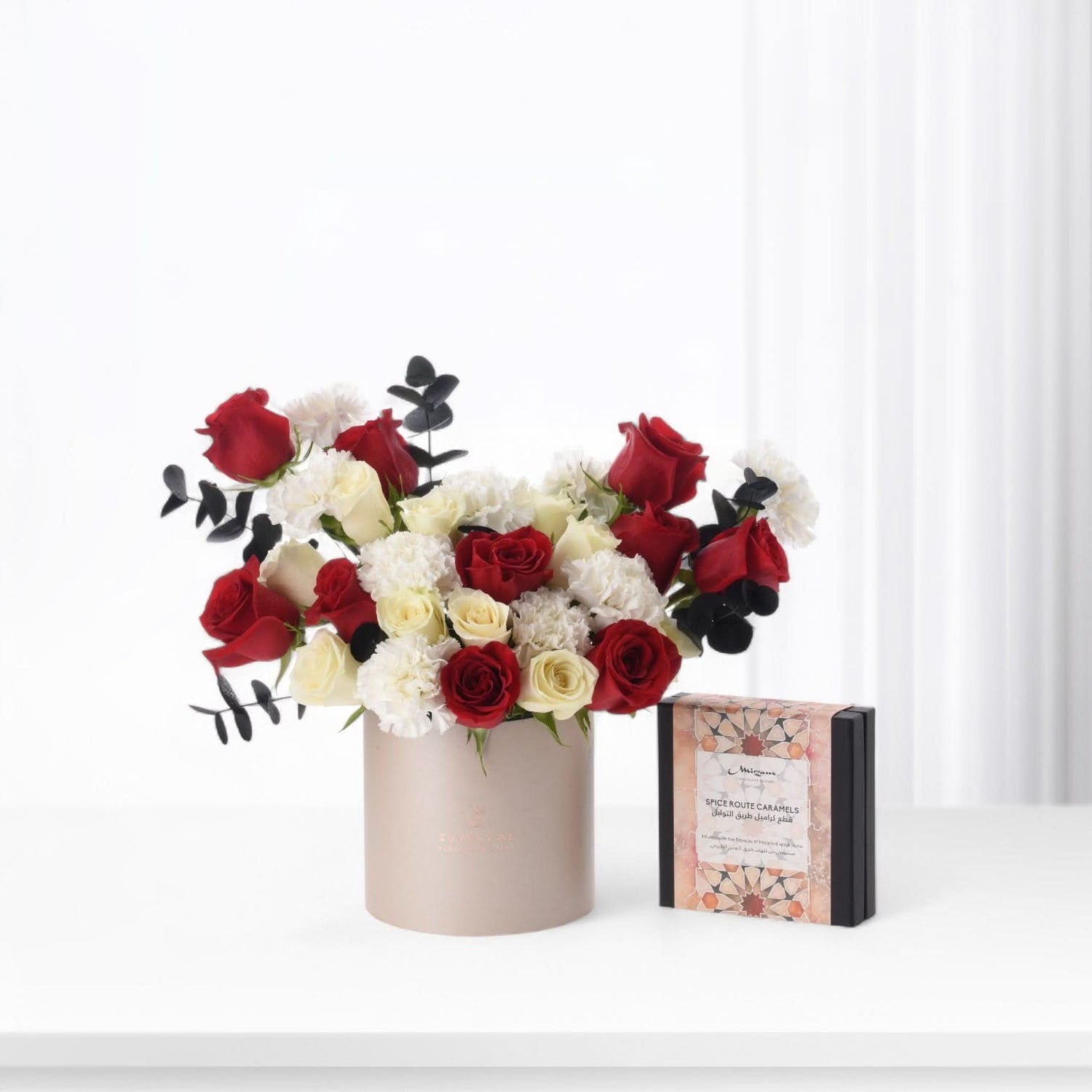 Elegant sand box arrangement with red and white roses from ZUVEES, paired with Luxe Chocolate, Mirzam, and Lakrids — a refined gift of sweetness and love.