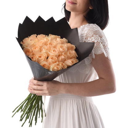 Soft peach roses in sleek black wrap, held by woman in lace dress.