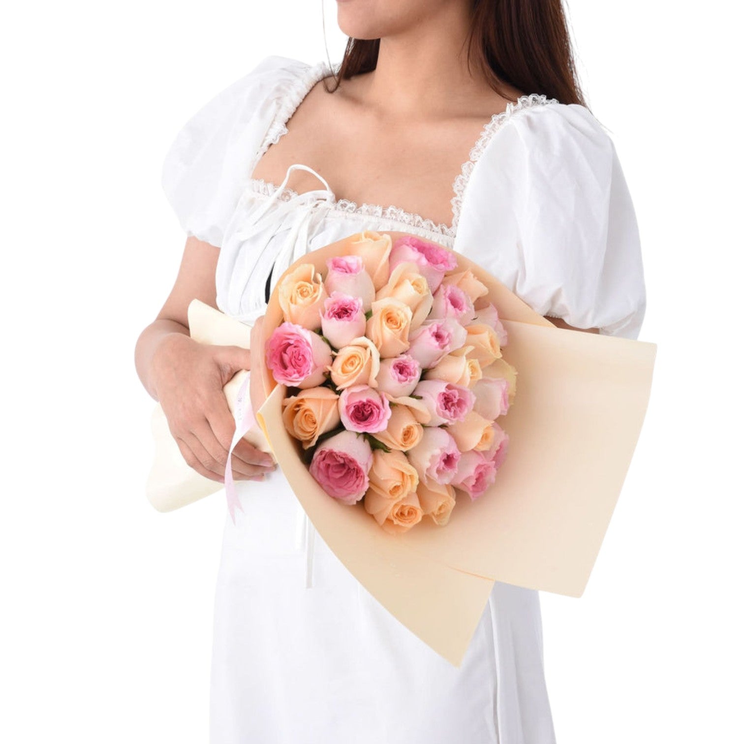 Soft pink and peach roses wrapped in cream paper, held by a woman in white.