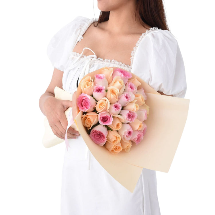 Soft pink and peach roses wrapped in cream paper, held by a woman in white.