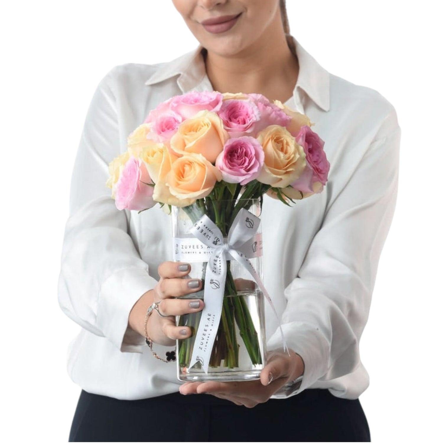 Woman holds clear vase with pastel pink and peach roses, branded ribbon.