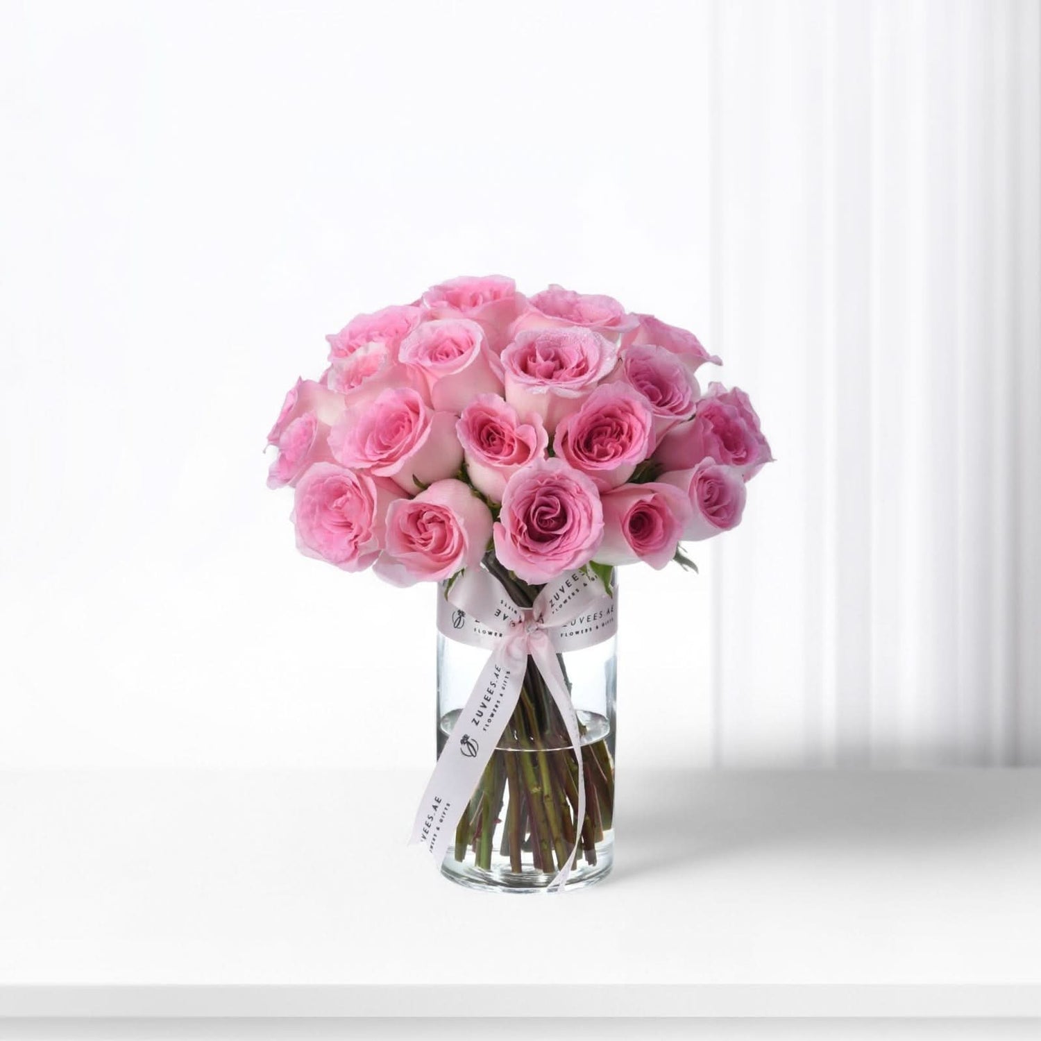 Pink roses in clear vase, ribbon-tied, soft light, elegant arrangement.
