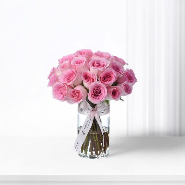 Pink roses in clear vase, ribbon-tied, soft light, elegant arrangement.