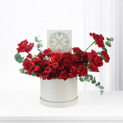 Luxurious red roses and carnations in elegant white box with gold-embossed card.