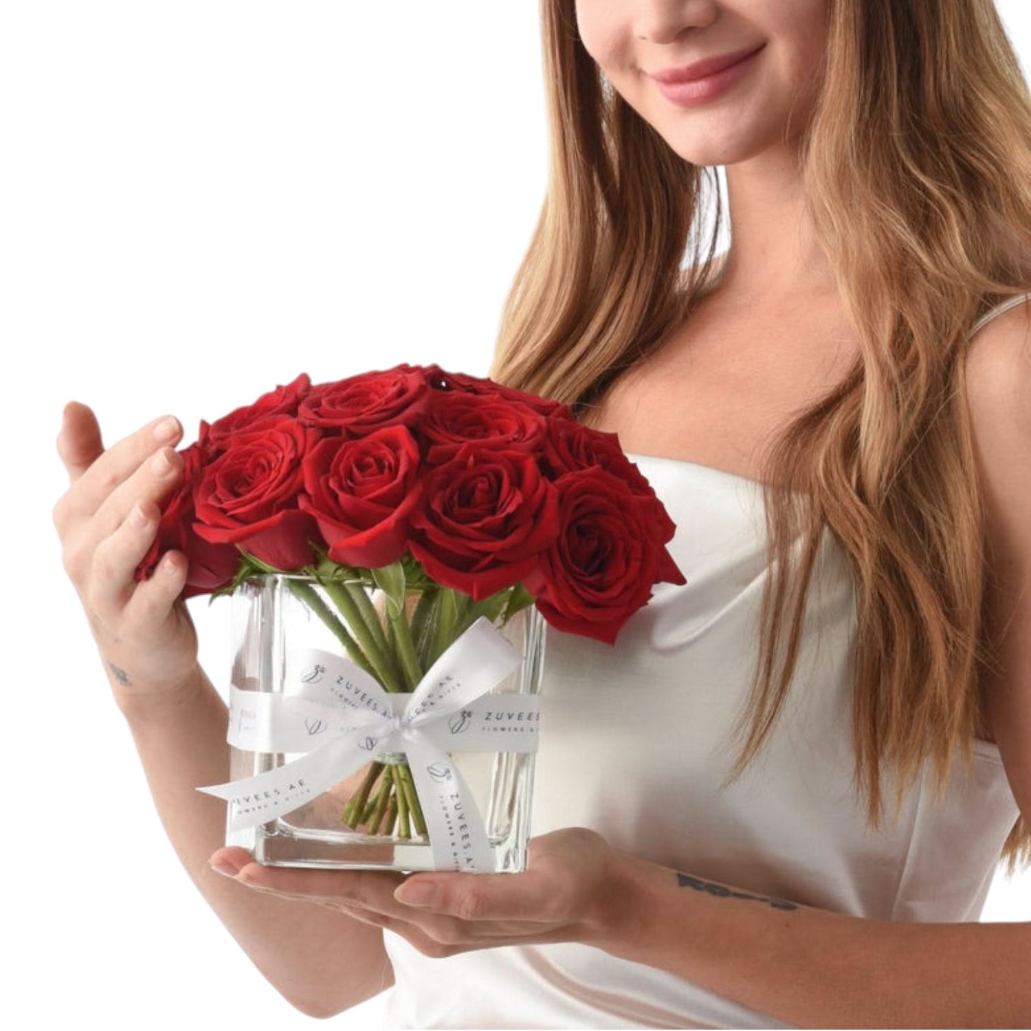 Vibrant red roses in clear glass vase with elegant white ribbon bow.