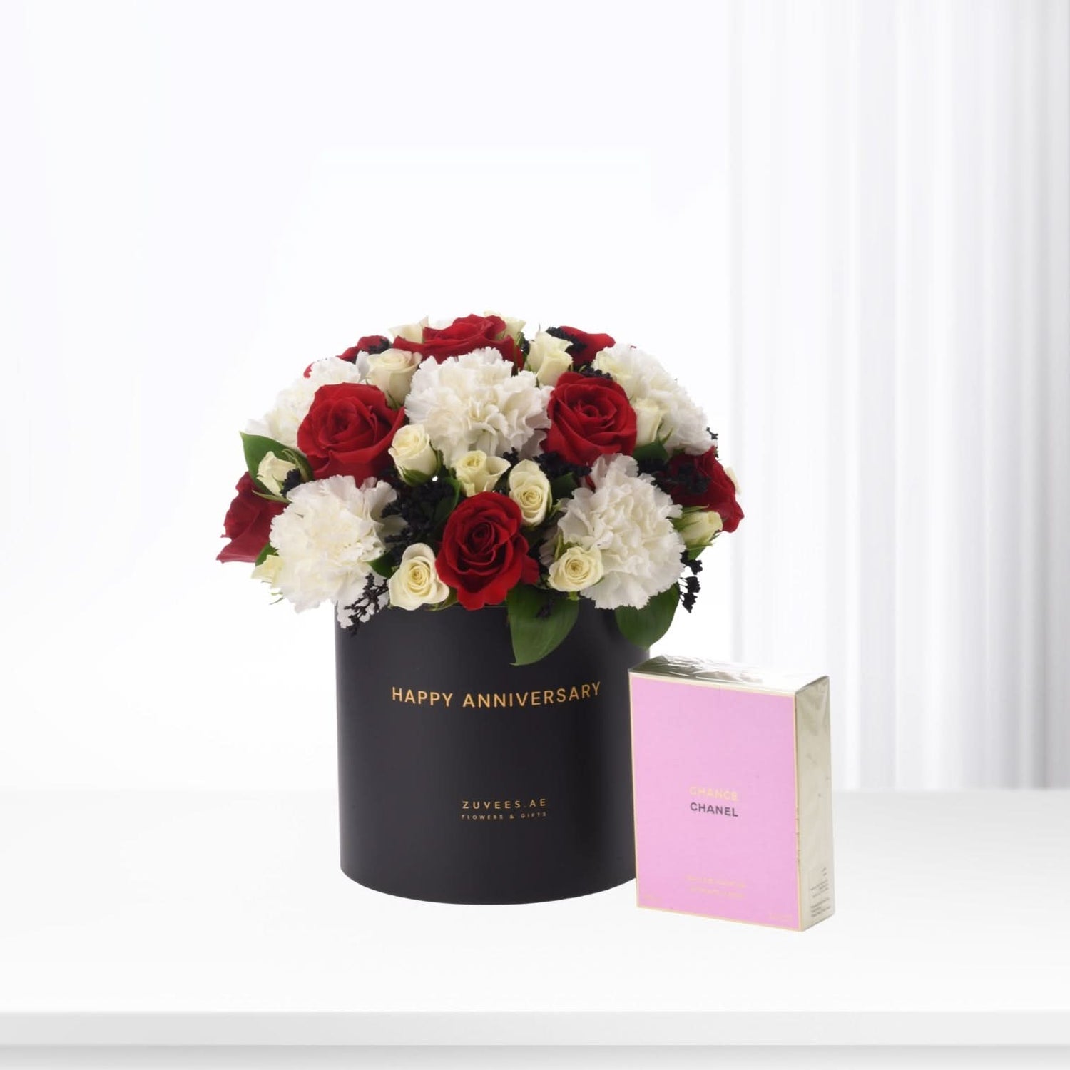 Elegant black hat box with red and white roses, beside pink Chanel perfume.