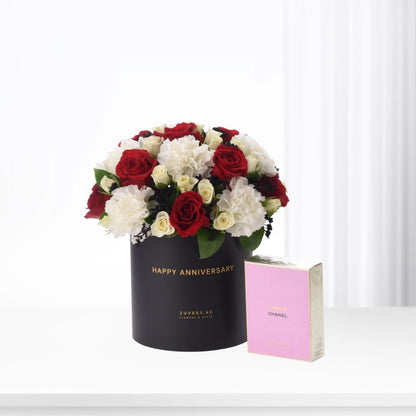 Elegant black hat box with red and white roses, beside pink Chanel perfume.