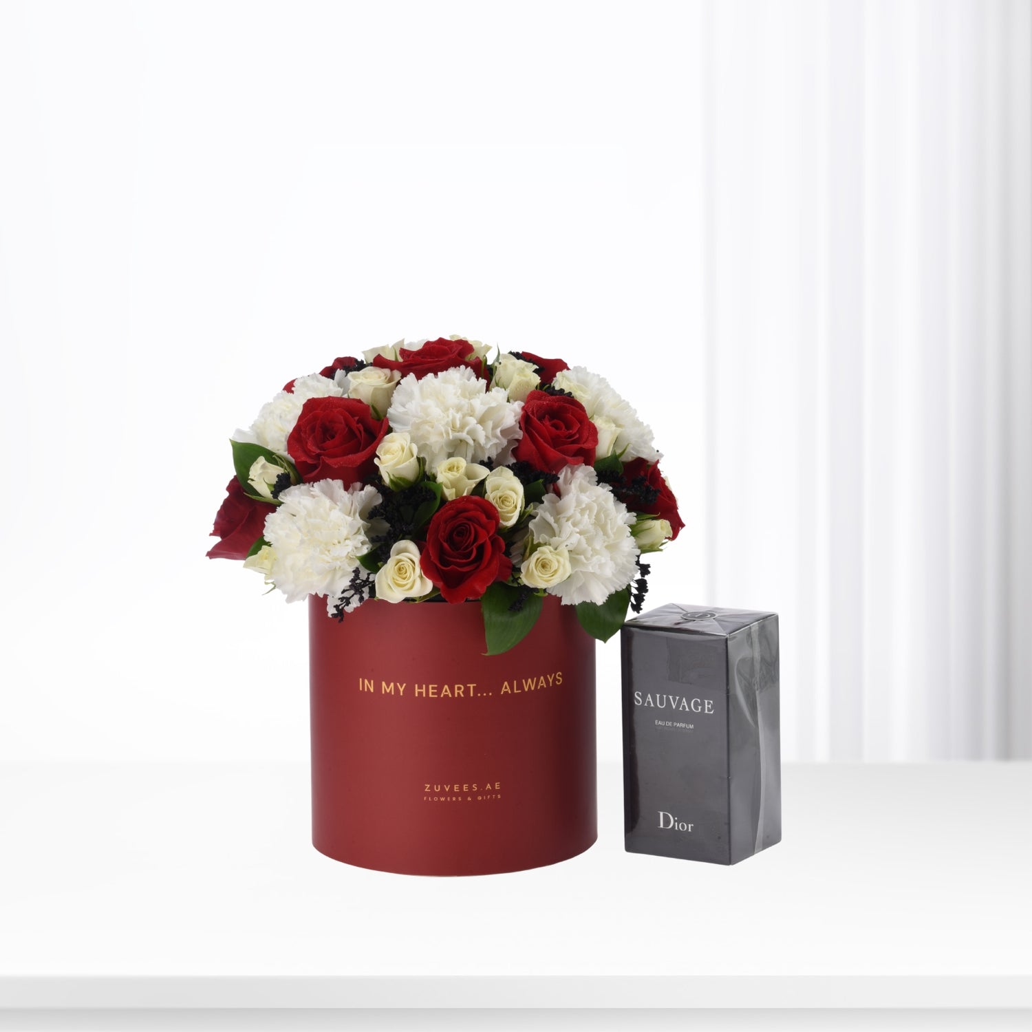 Red cylindrical box with red and white roses, beside Dior Sauvage perfume.