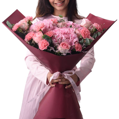 Pink roses, carnations, and hydrangeas wrapped in burgundy paper with ribbon.