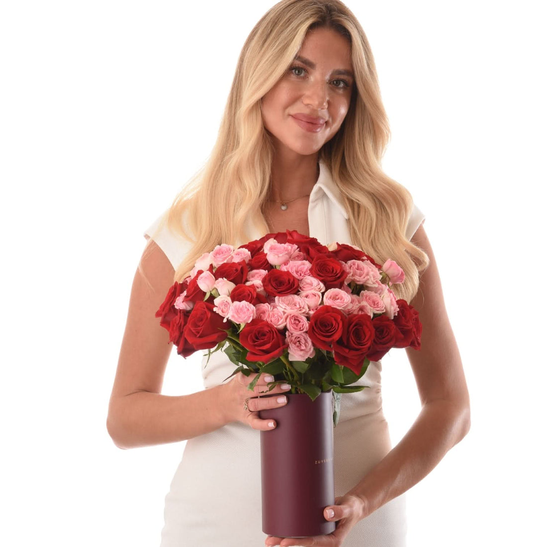 Woman holds lush red and pink roses in sleek burgundy vase.