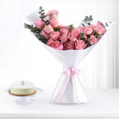 Soft pink roses in white paper, tied with ribbon, beside a delicate cake.