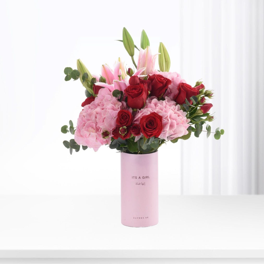 Pink vase holds red roses, pink hydrangeas, and lilies for baby girl celebration.