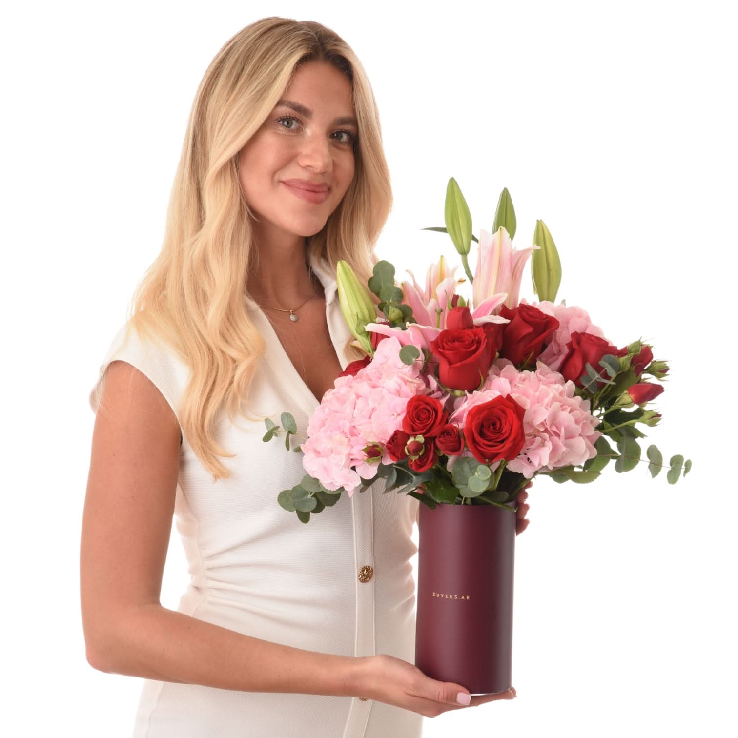 Woman holds elegant bouquet of red roses, pink hydrangeas, and lilies in matte burgundy vase.