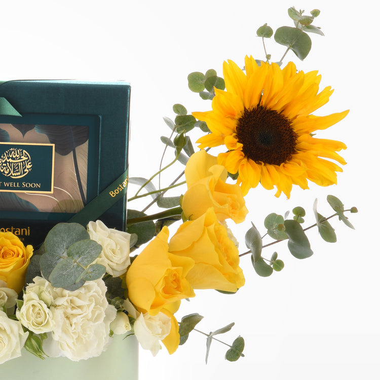 Vibrant sunflower, yellow and white roses with eucalyptus, beside teal "Get Well Soon" gift box.