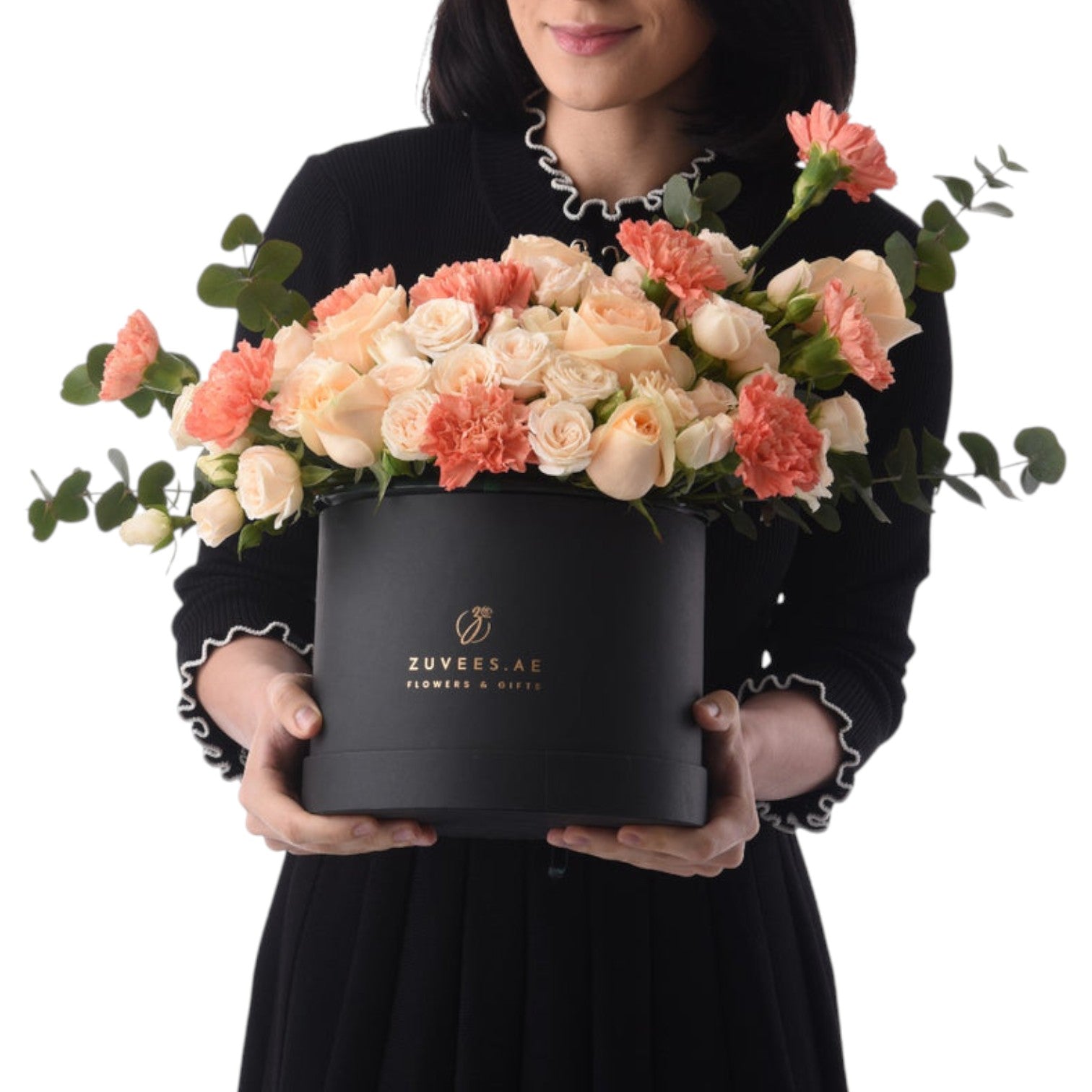 Elegant black hat box filled with peach roses and carnations, held by a woman.