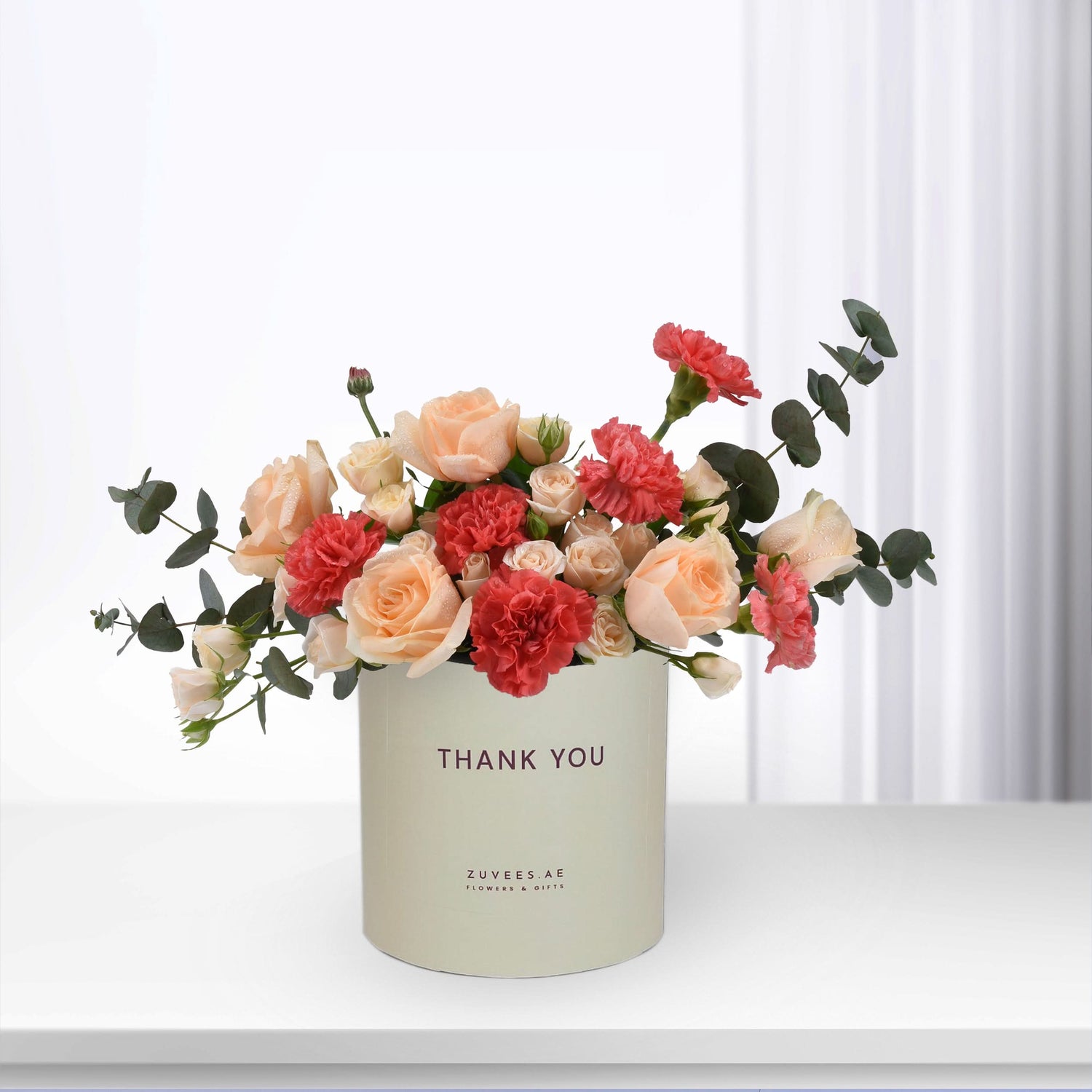 Pastel peach roses and red carnations in cream box with "Thank You" text.