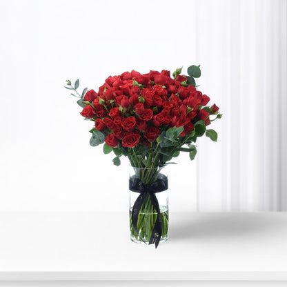 Vibrant red roses in clear vase, accented with black ribbon and eucalyptus.