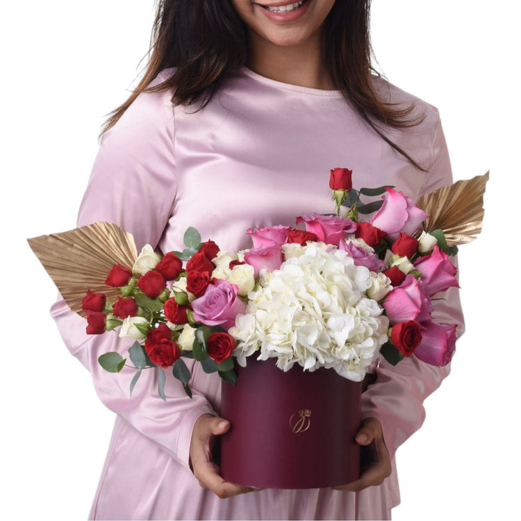 Woman holds burgundy box with red, pink, and white roses and hydrangeas.