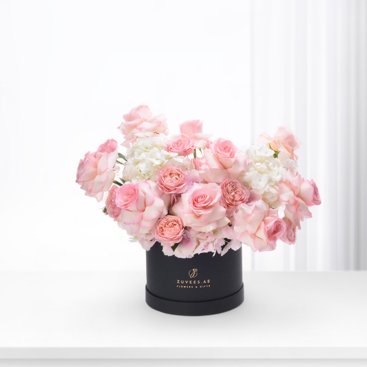 Elegant pink roses and hydrangeas in sleek black box with gold logo.