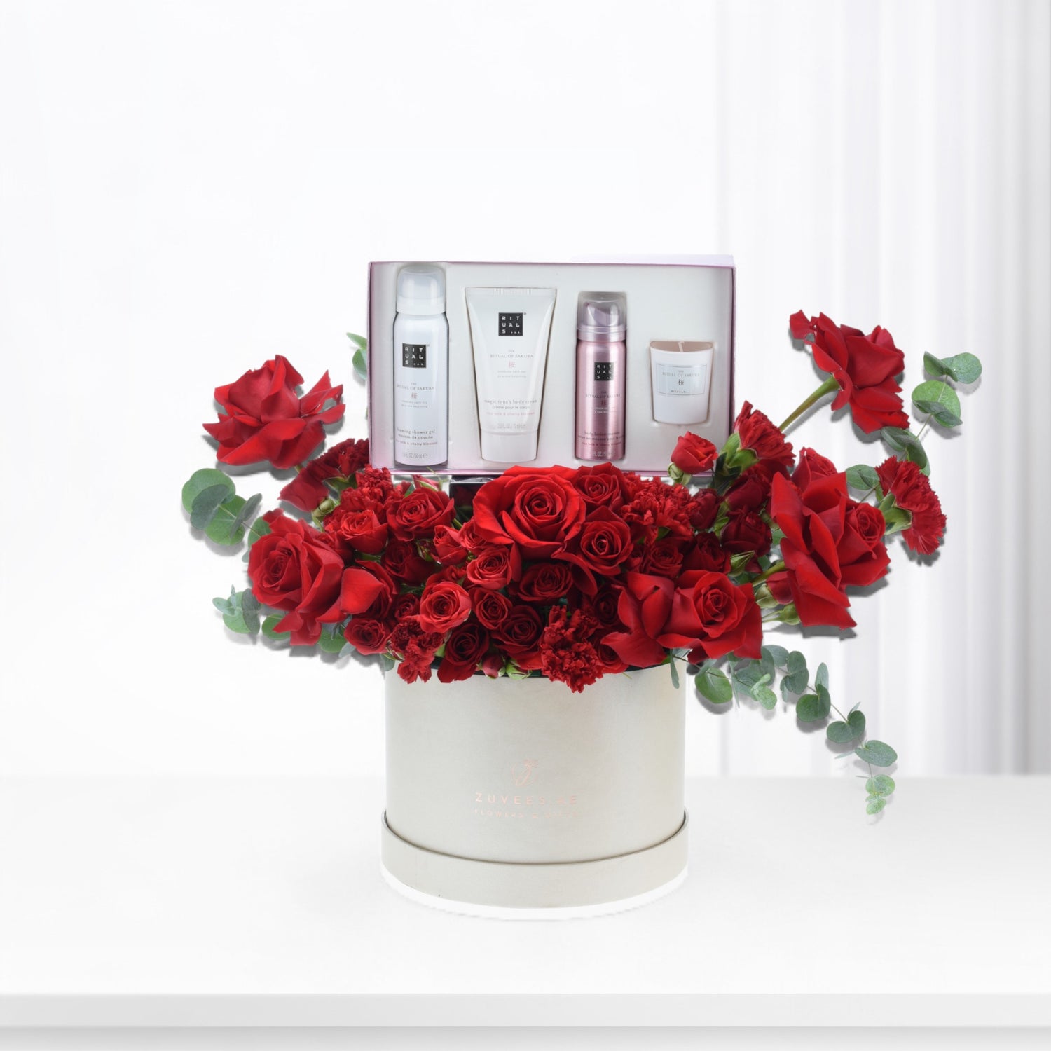 Luxurious red roses cascade around a white gift box with Rituals skincare, elegantly presented.